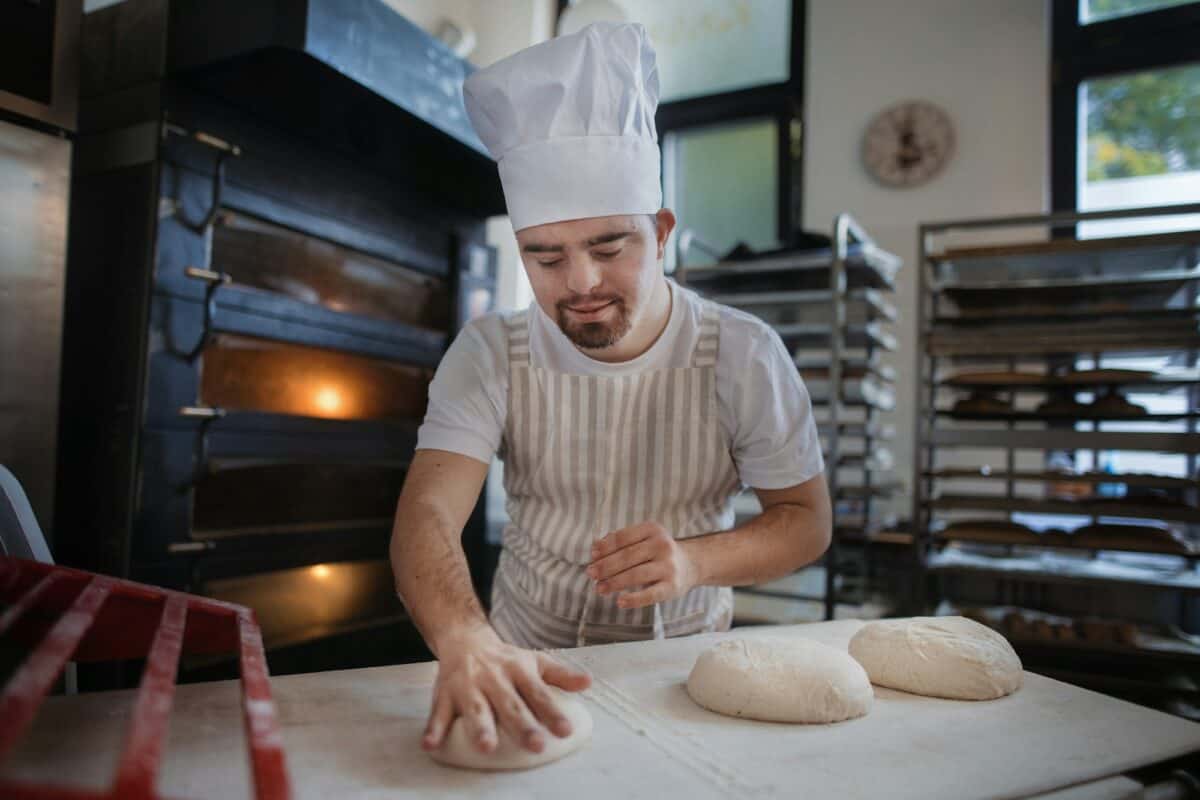 Jeune boulanger atteint du syndrome de Down préparant des pâtisseries dans une boulangerie. Concept d'intégration des personnes atteintes